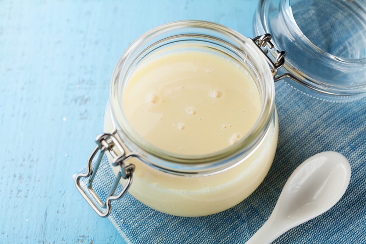 Glass jar with condensed milk or evaporated milk on blue rustic table.