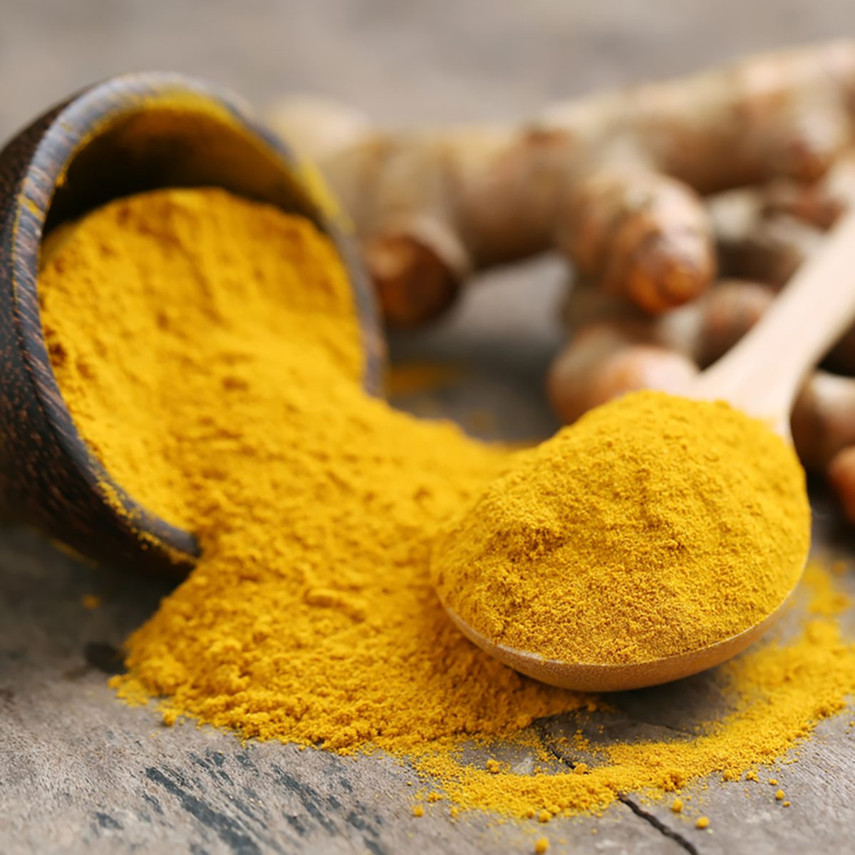 Turmeric powder and fresh turmeric on wooden background.
