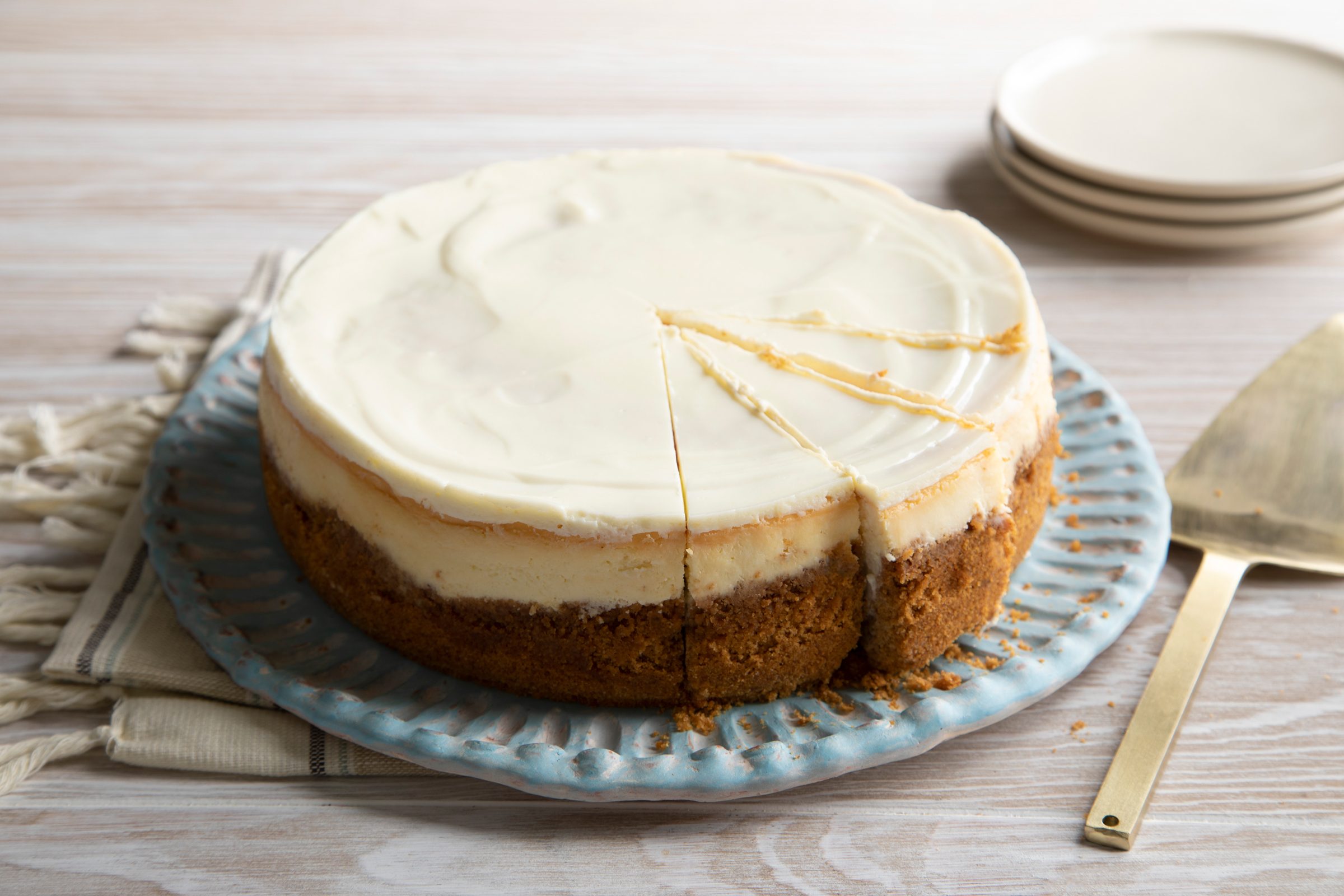 a whole plain cheesecake with part of the cheesecake cut into slices