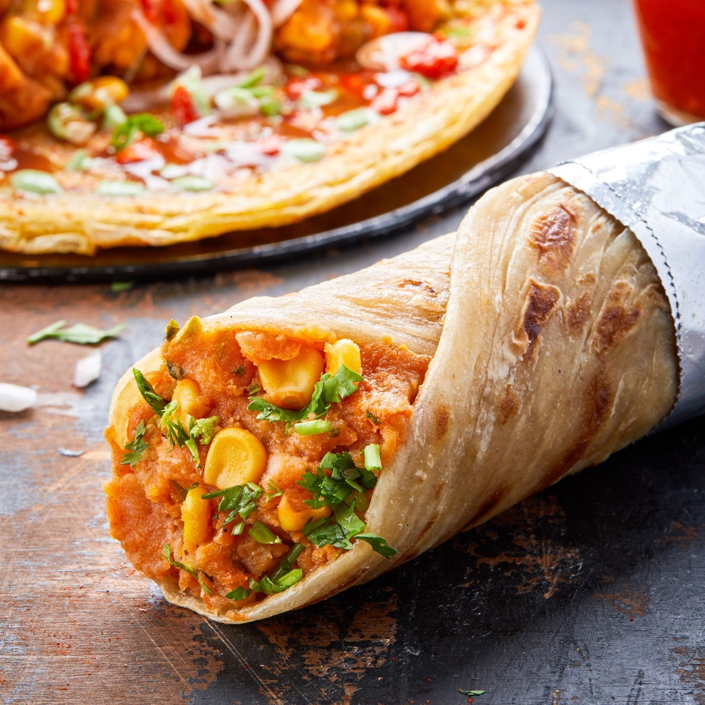 Kati roll with vegies on a table against sauces and other rolls in the background