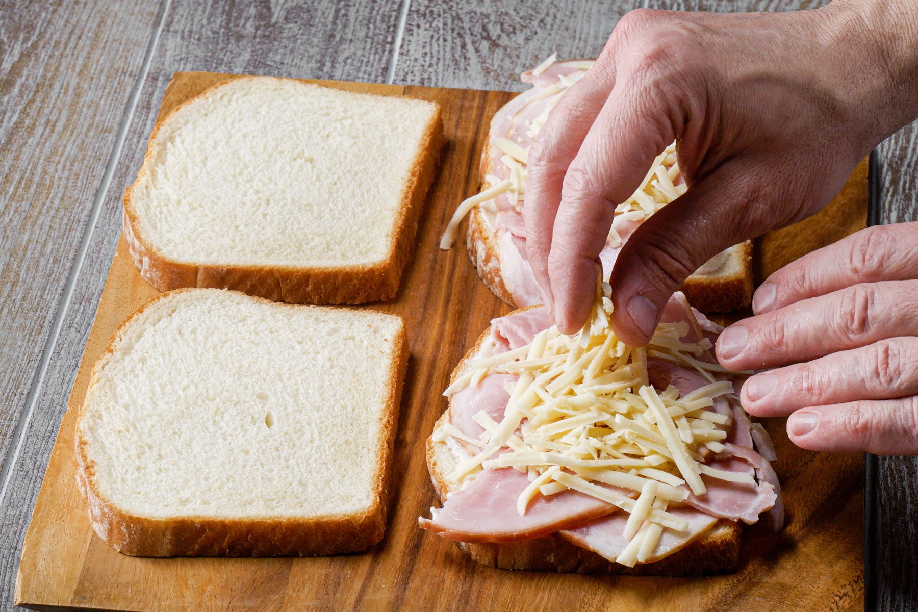 Layering the bread with ham and cheese on a wooden tray
