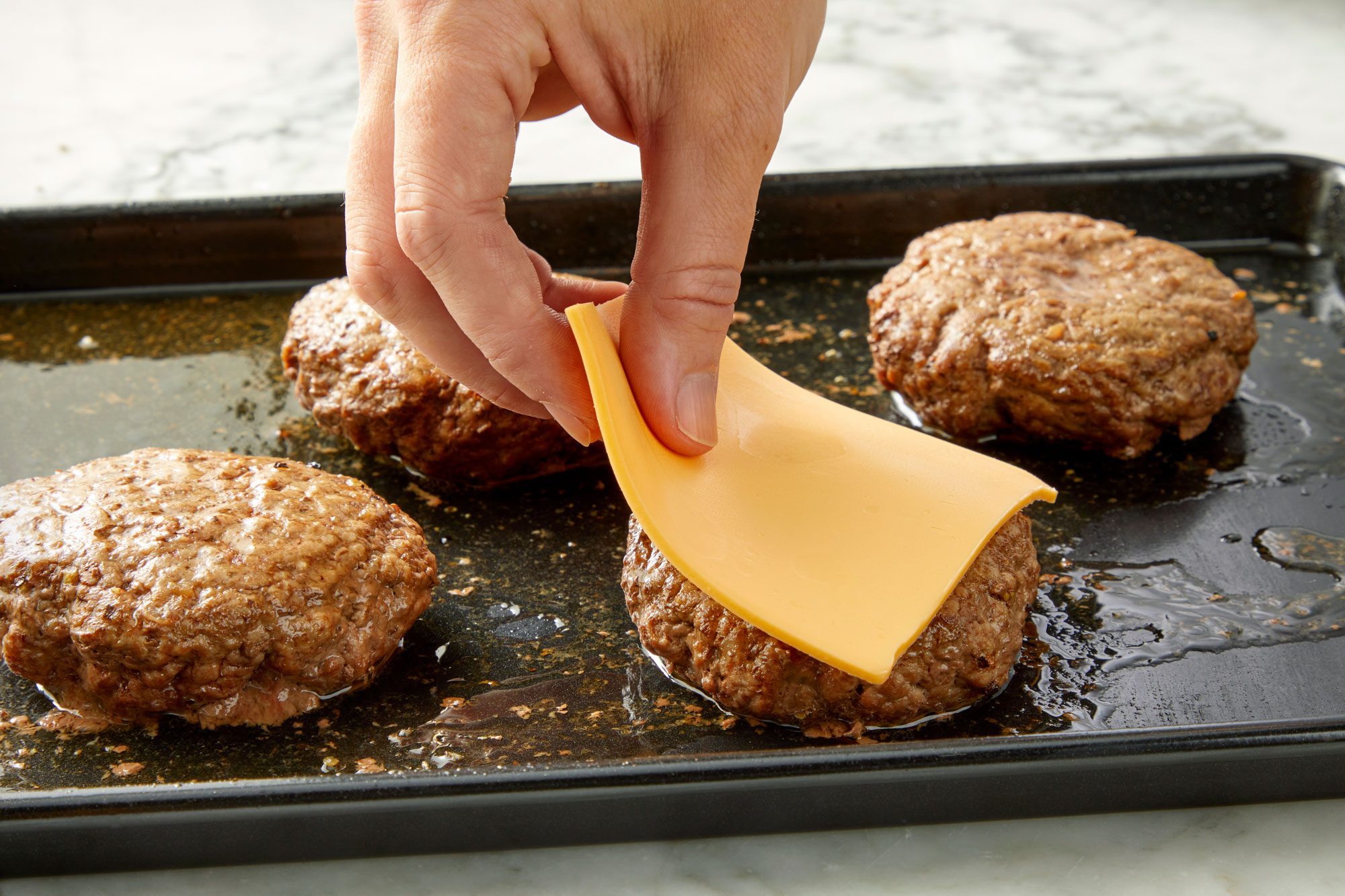 3/4 angle view shot of top each patty with cheese during the last 2-3 minutes; baking sheet; marble background;