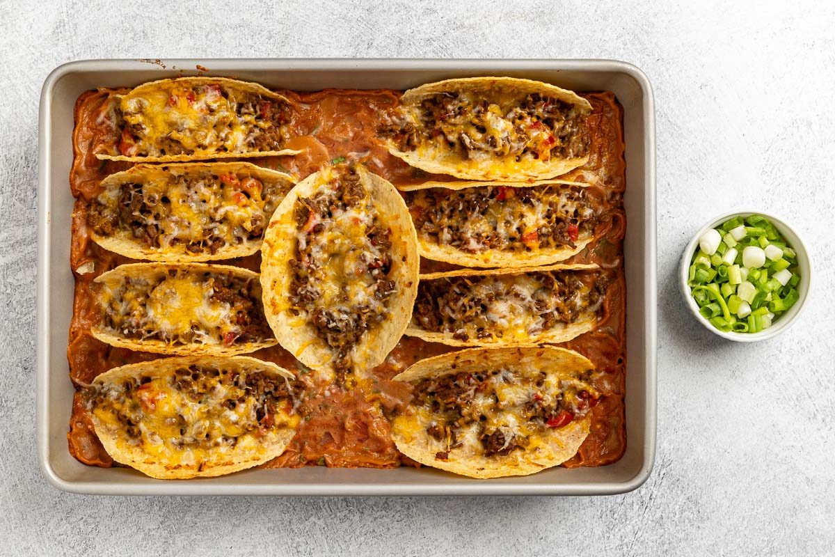 Taste of Home Baked Tacos recipe photo of the baked tacos topped with melted cheese and a side of green onions.
