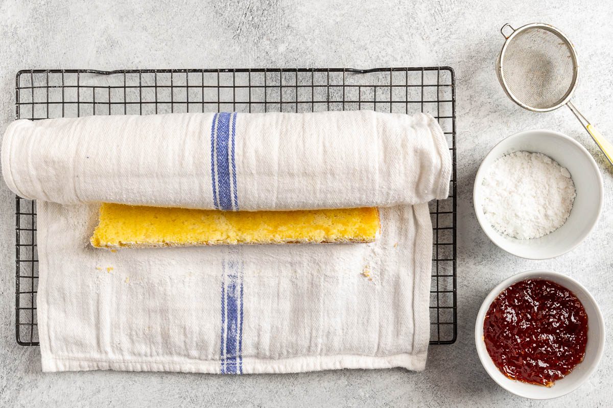 Taste of Home Jelly Roll recipe photo of the baked cake rolled in towl with confectioner's sugar and jelly to finish.