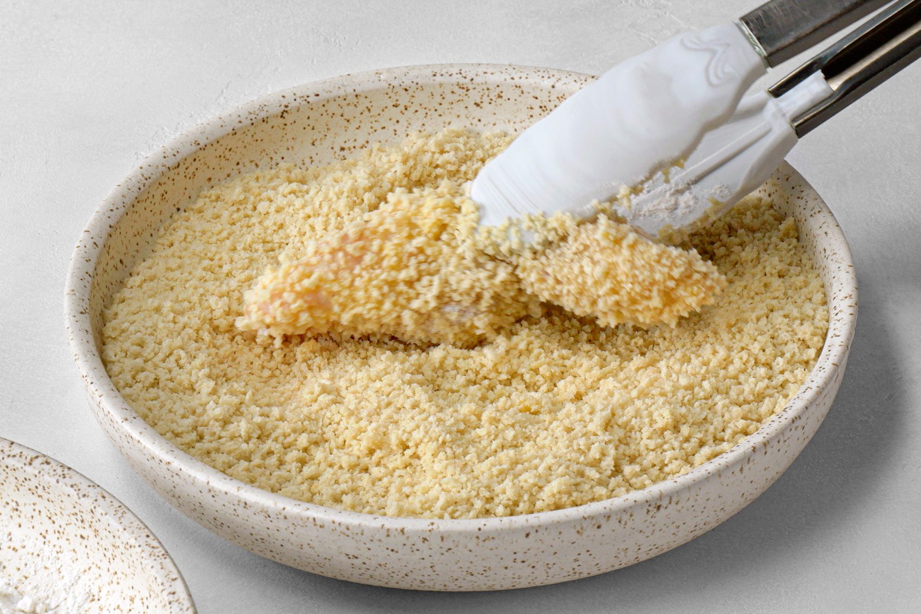 tongs being used to hold fish and coat it in panko