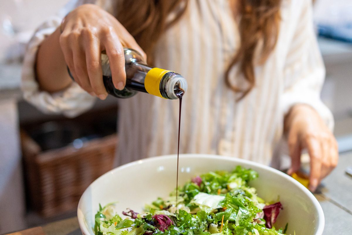 Female hand pouring balsamic vinegar on the fresh vegetables salad