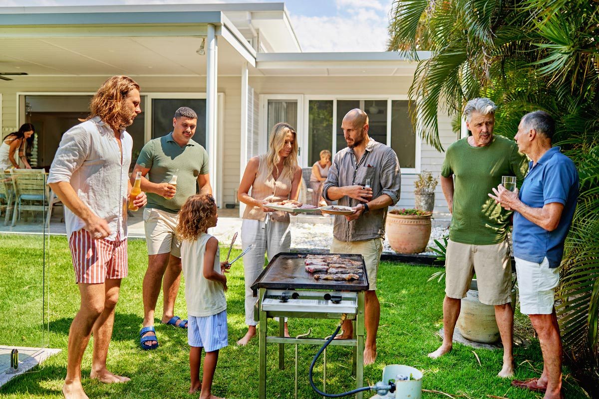 Casually dressed men and women ranging in age from 7 to 76 years preparing food, setting patio table, and conversing.