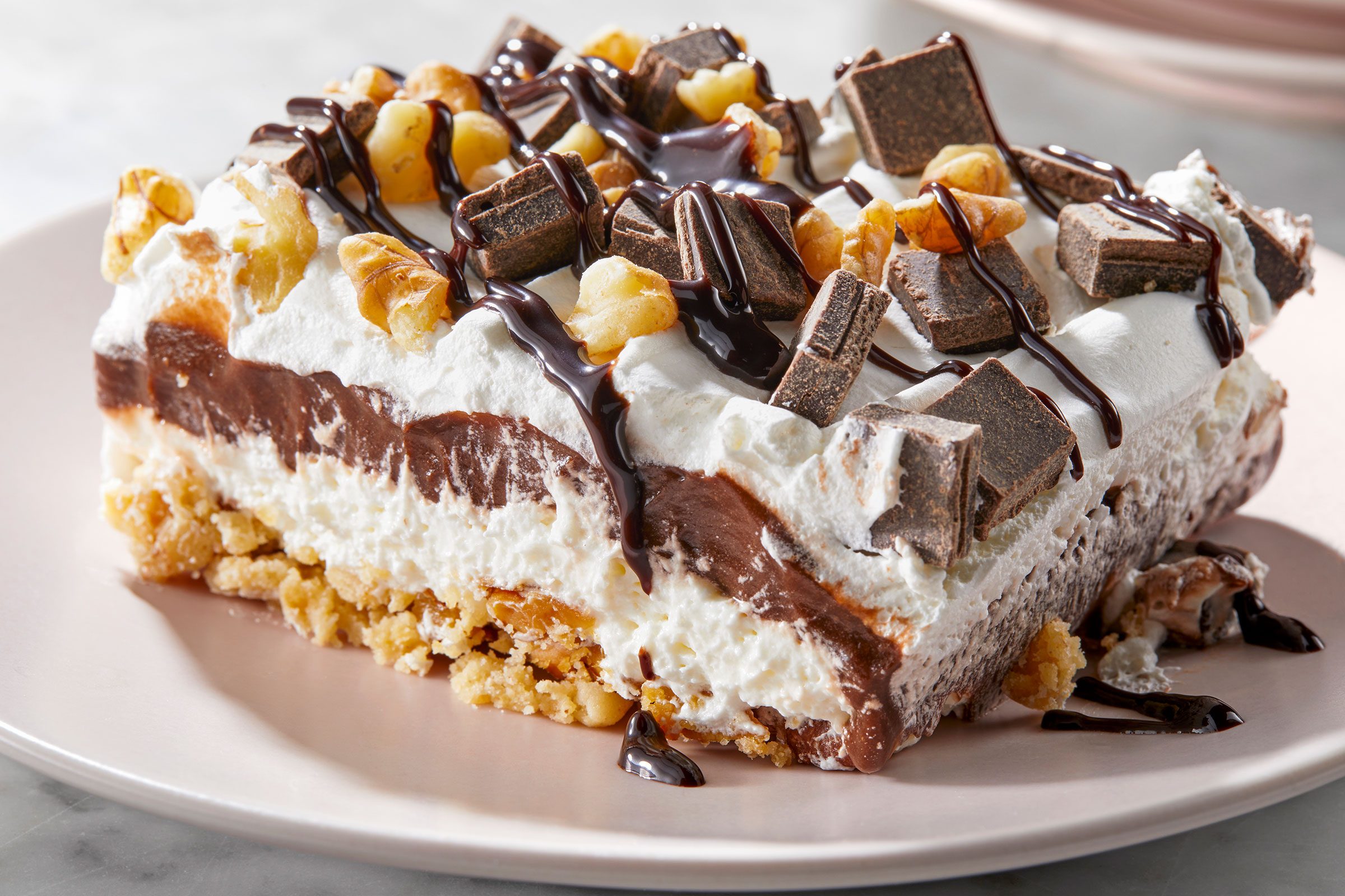 A piece of chocolate delight chocolate pudding with whipped cream and chunks of chocolate and walnuts.